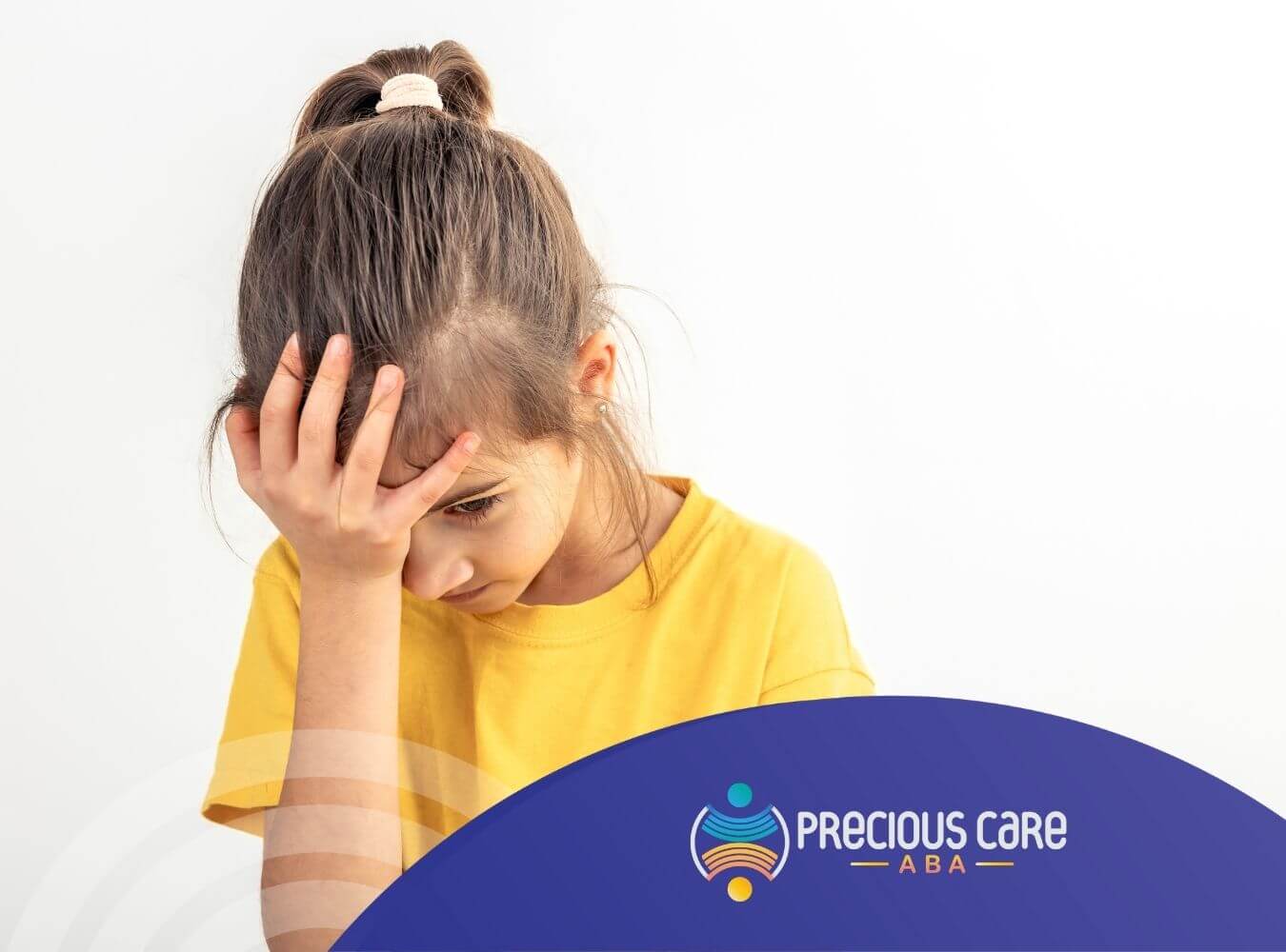A girl looks down in frustration during ABA, holding her forehead with one hand.