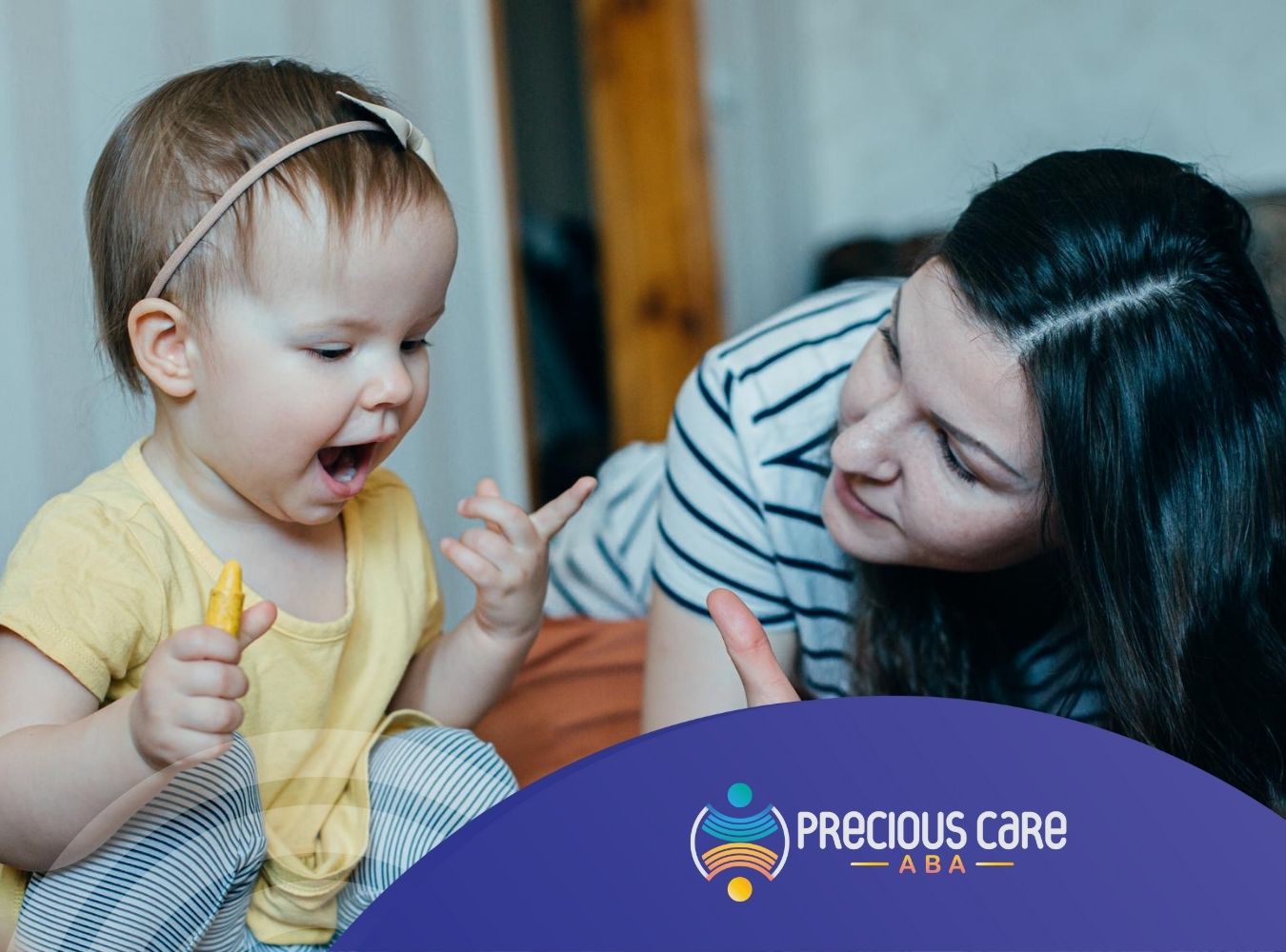 A smiling toddler holding a yellow crayon, receiving encouragement from an ABA therapist.
