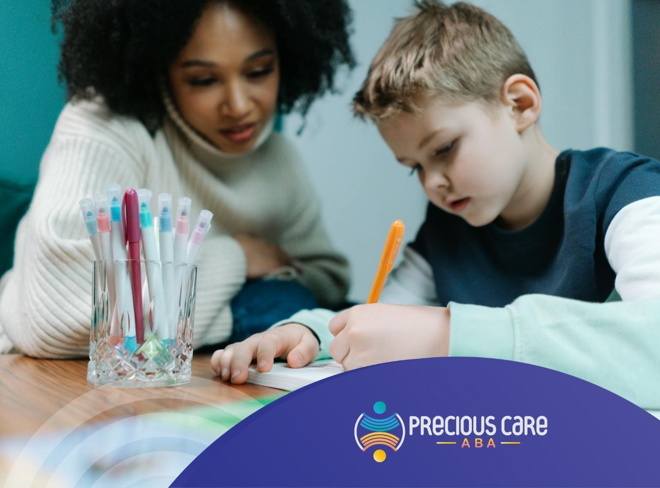 Autistic boy writing on paper with an RBT assisting him at table with colorful markers in Colorado.