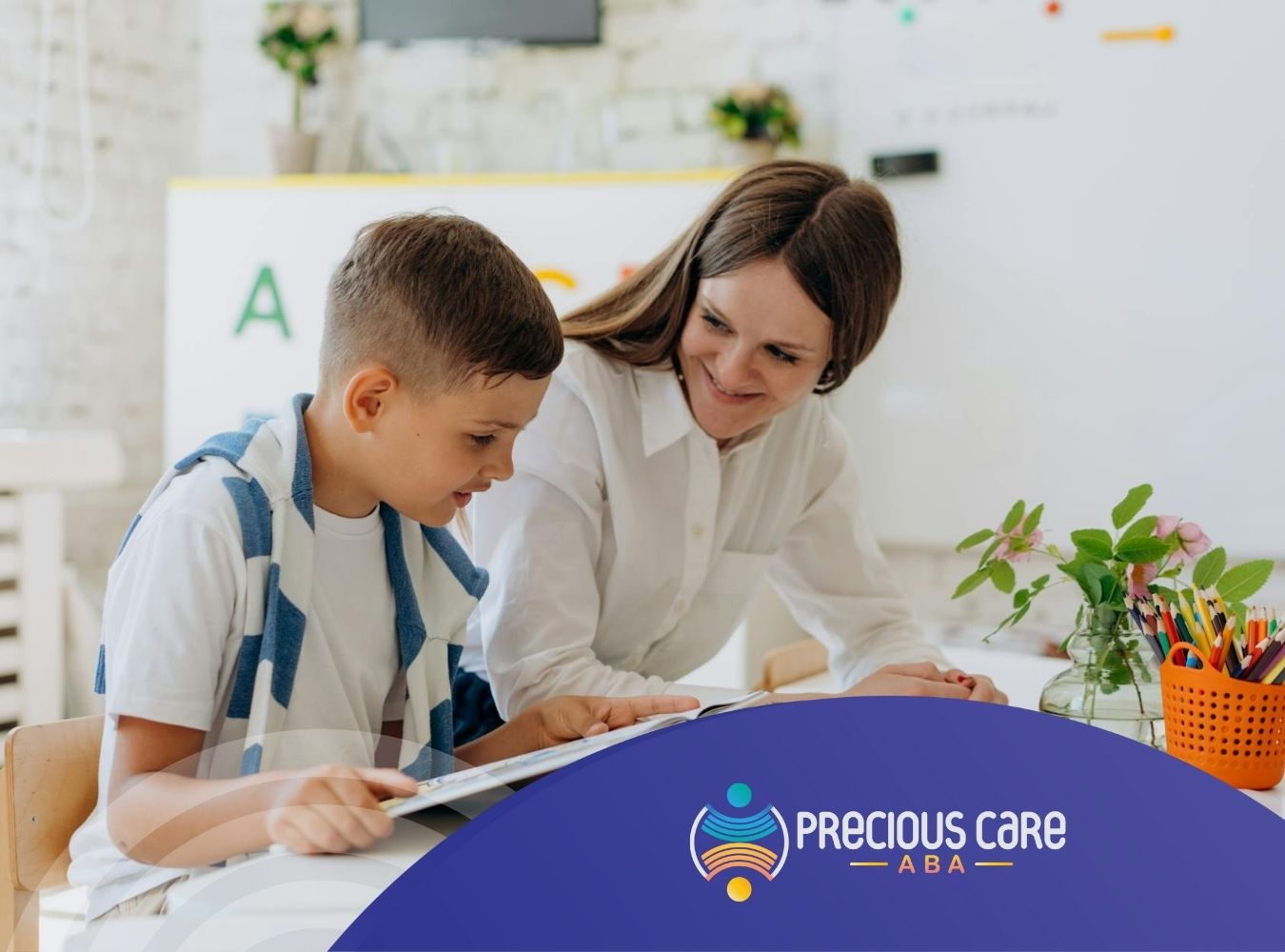 An ABA therapist and autistic boy sitting at a table, reading a book together at a classroom in CO.