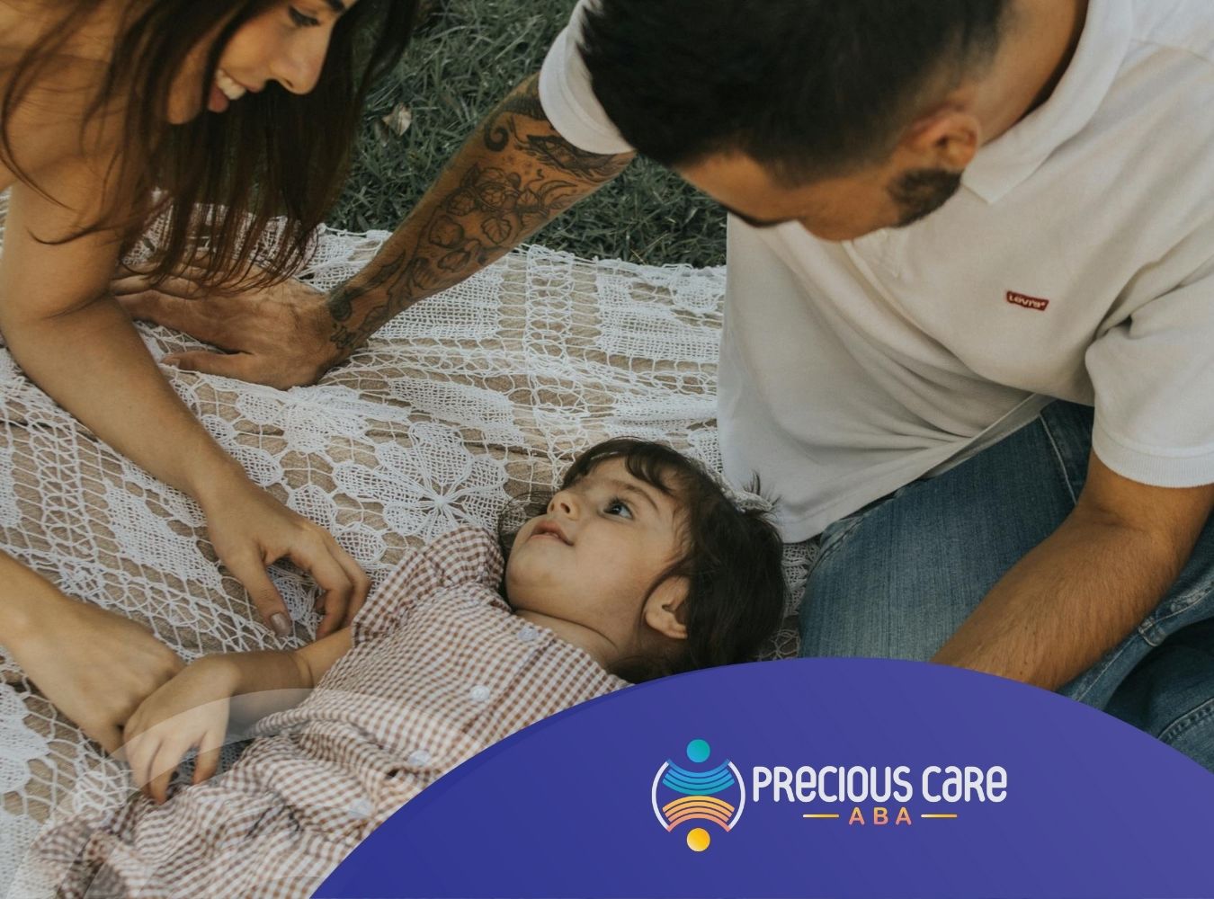 Parents playing with their autistic daughter on a picnic blanket outdoors, sharing a joyful moment.