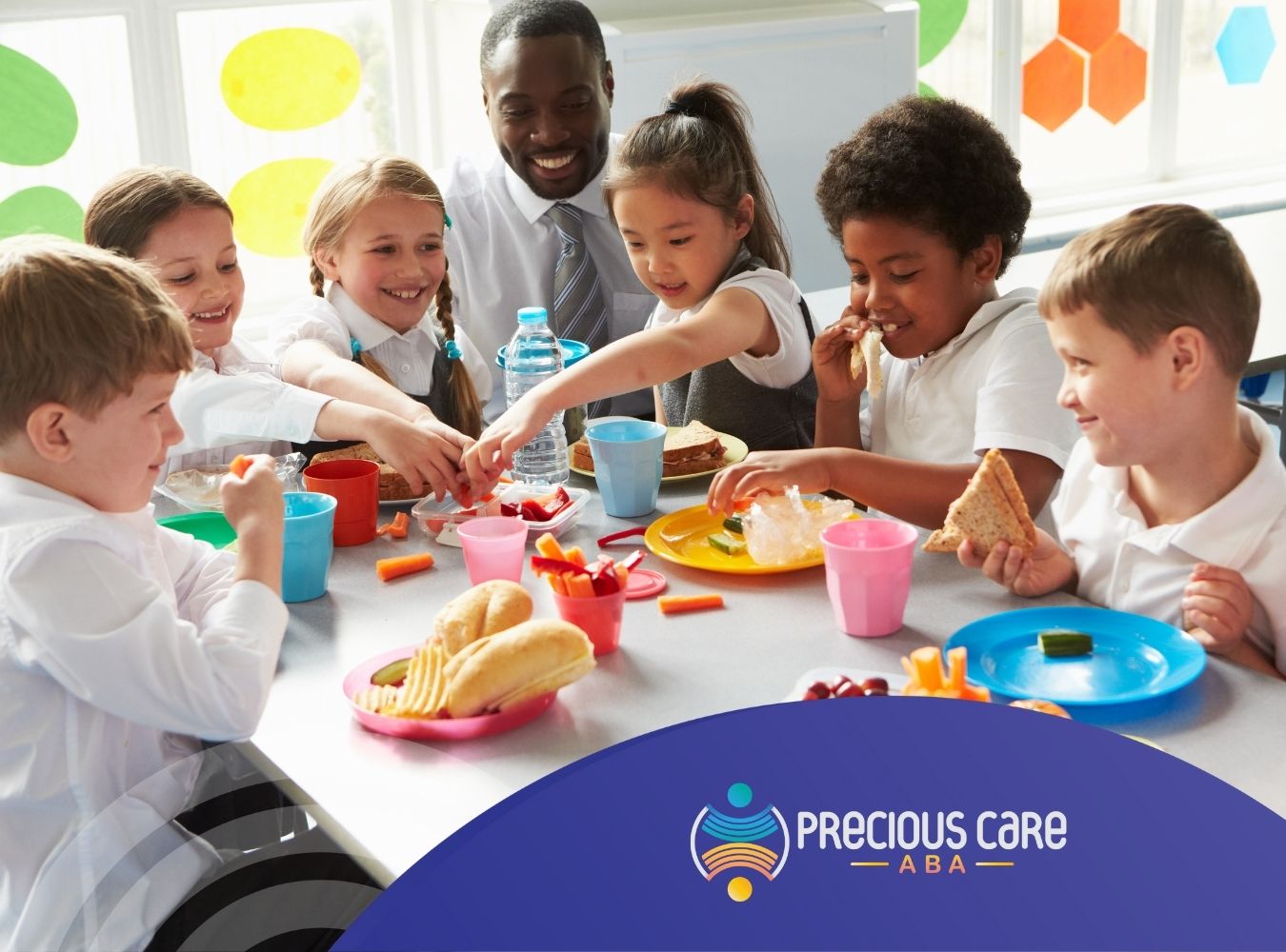 A group of children eating on a table, at school, with their teacher.