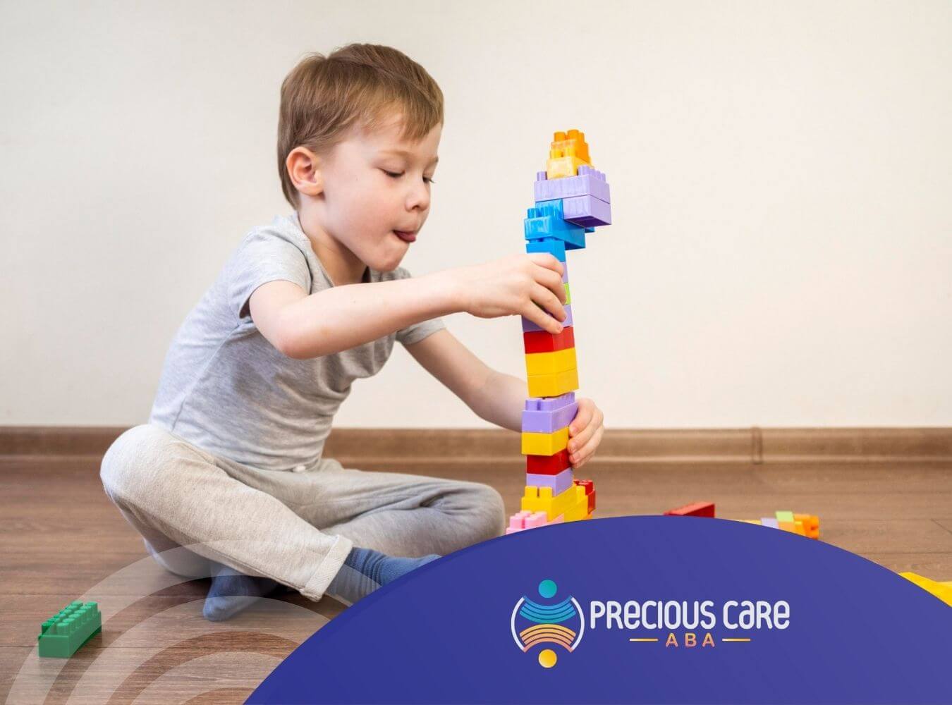 A young boy with is focused on stacking colorful building blocks into a tall structure in ABA therapy.