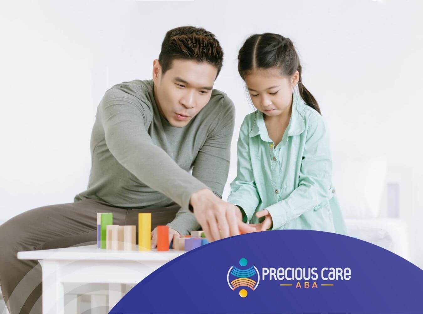 An ABA therapist and a young girl building with colorful blocks on a table in ABA therapy.