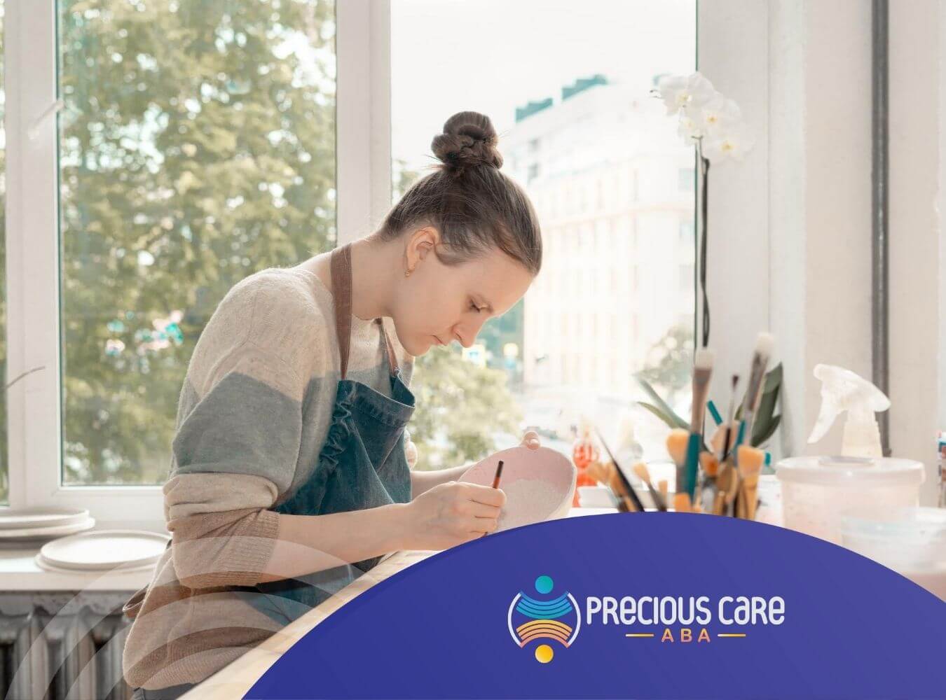 Woman with autism pottery at a table with brushes and art supplies.