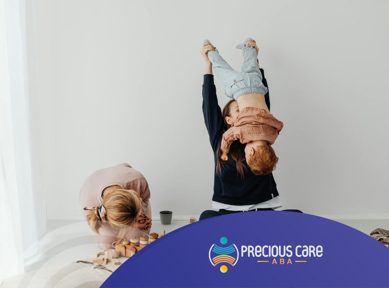 Parent lifting a laughing autistic child upside down while another plays with toys during in-home ABA therapy in MD.
