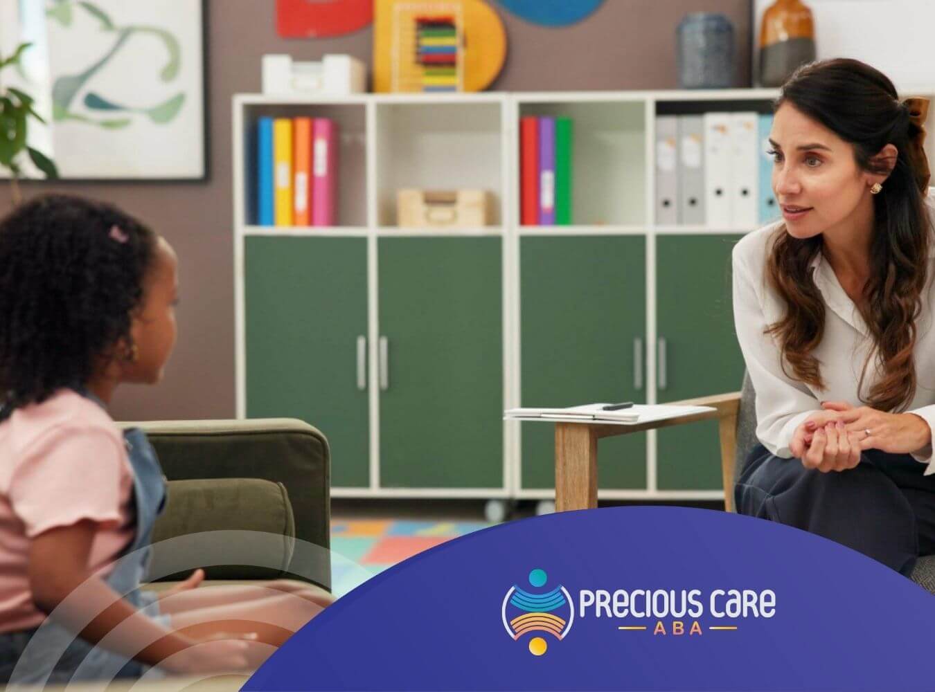 BCBA talking with autistic child in playroom during ABA therapy session.